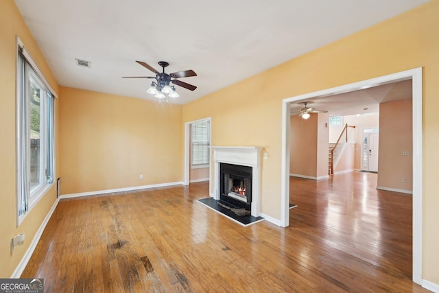 unfurnished living room with baseboards, a lit fireplace, visible vents, and wood finished floors