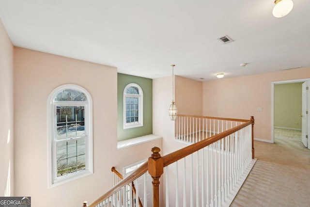 corridor with light colored carpet, baseboards, visible vents, and an upstairs landing