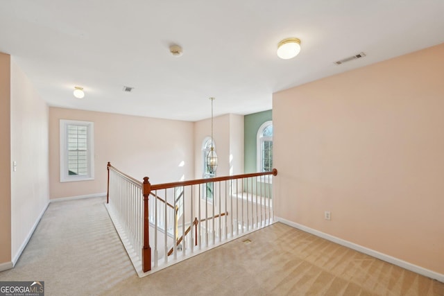 hallway with baseboards, a chandelier, visible vents, and light colored carpet