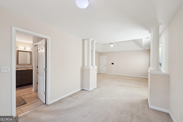 empty room with light carpet, decorative columns, baseboards, and ceiling fan