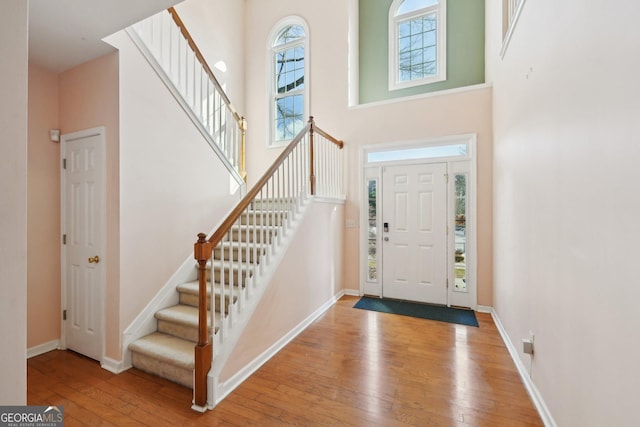 entryway with light wood-style flooring, a high ceiling, baseboards, and stairs