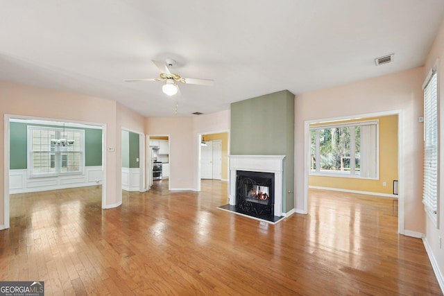 unfurnished living room featuring light wood-style flooring, visible vents, ceiling fan, and a lit fireplace