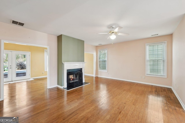 unfurnished living room with a lit fireplace, wood finished floors, and visible vents