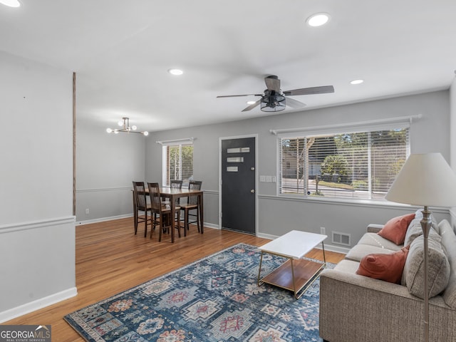 living room featuring ceiling fan with notable chandelier and hardwood / wood-style flooring