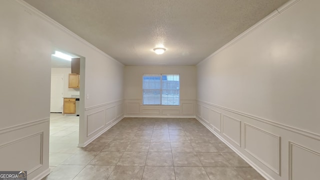 empty room with light tile patterned floors, a textured ceiling, and ornamental molding