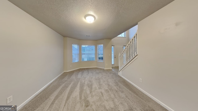 spare room featuring light colored carpet and a textured ceiling