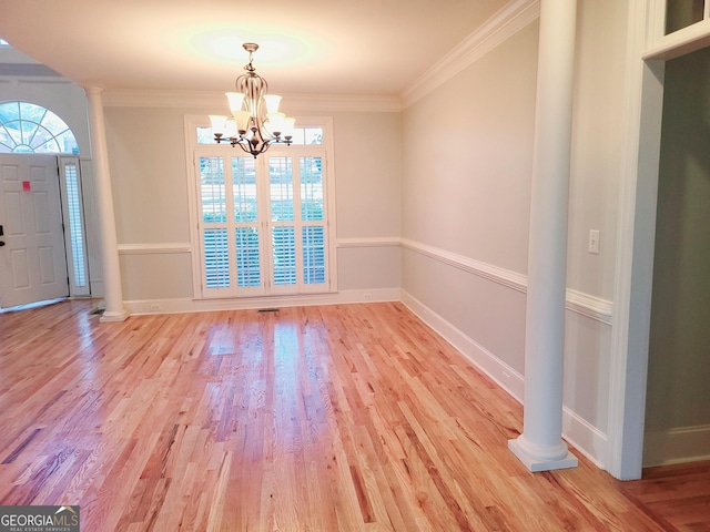 foyer entrance featuring light hardwood / wood-style floors, an inviting chandelier, ornamental molding, and ornate columns