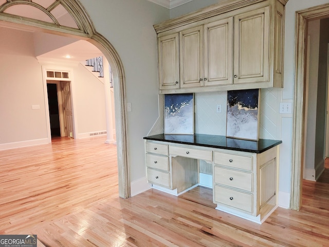 unfurnished office featuring crown molding, built in desk, and light wood-type flooring