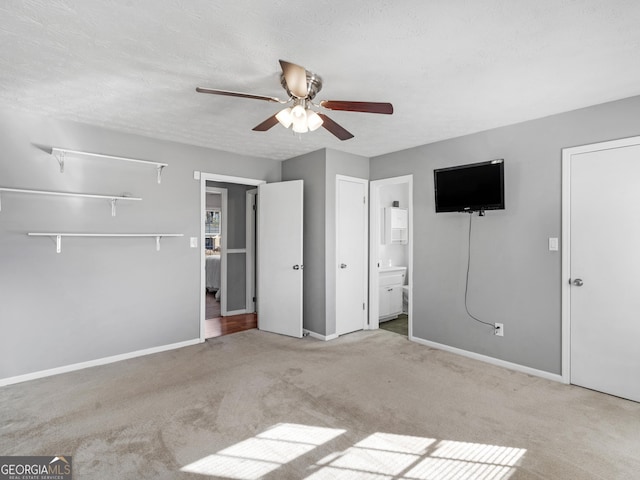 unfurnished bedroom with a textured ceiling, light colored carpet, ensuite bathroom, and ceiling fan