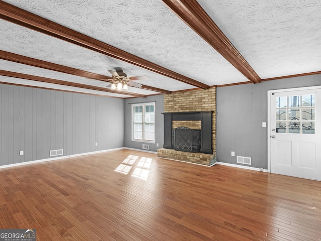 unfurnished living room featuring a fireplace, hardwood / wood-style flooring, a textured ceiling, and beamed ceiling