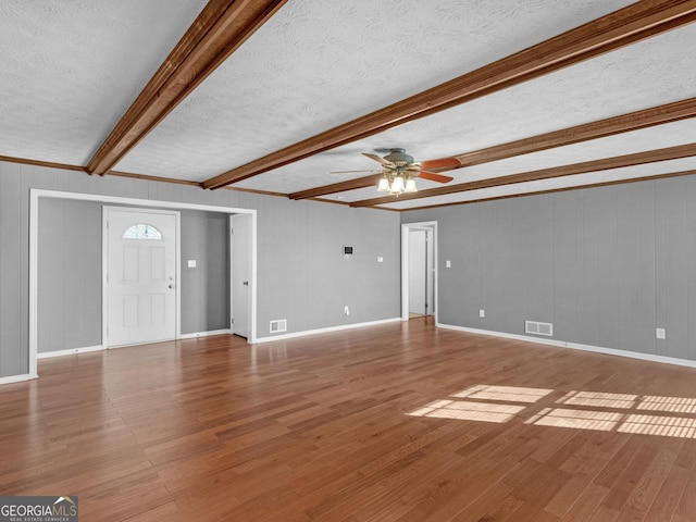 unfurnished living room featuring ceiling fan, beamed ceiling, a textured ceiling, and wood-type flooring