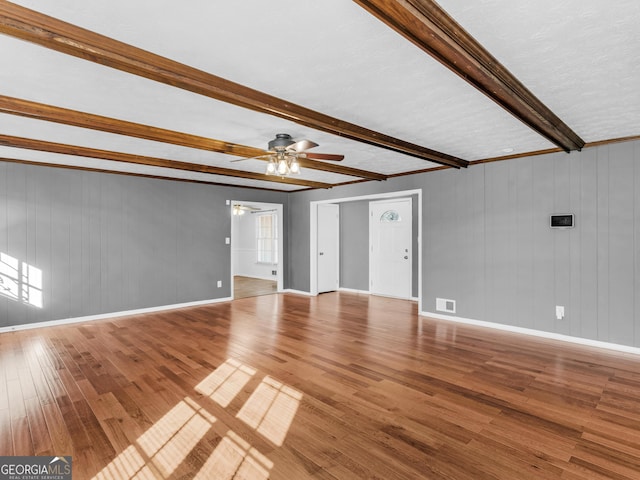 unfurnished living room featuring wood-type flooring, a textured ceiling, beamed ceiling, and ceiling fan