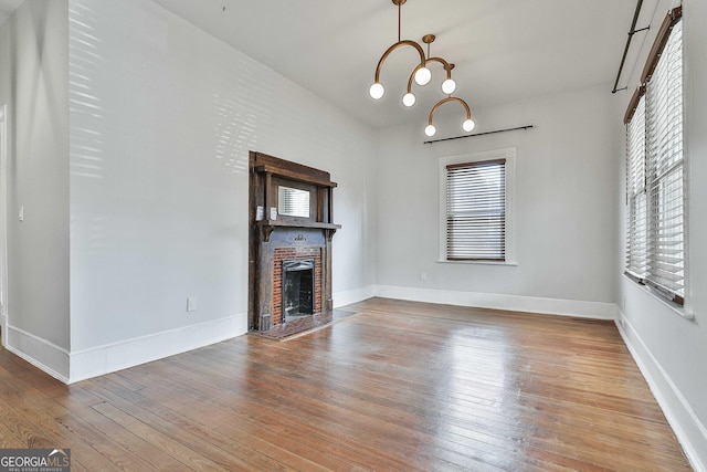 unfurnished living room featuring an inviting chandelier, hardwood / wood-style flooring, and a brick fireplace