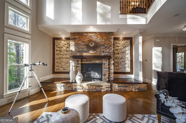 living room featuring ornamental molding, a stone fireplace, a towering ceiling, and hardwood / wood-style floors