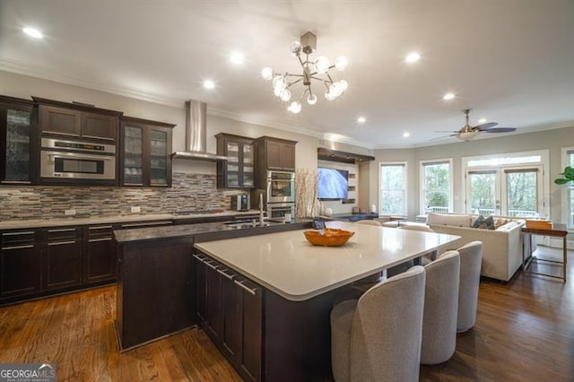 kitchen featuring a large island, sink, dark brown cabinetry, decorative backsplash, and wall chimney exhaust hood