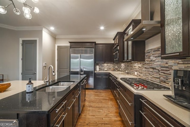 kitchen featuring appliances with stainless steel finishes, tasteful backsplash, sink, a kitchen island with sink, and wall chimney exhaust hood