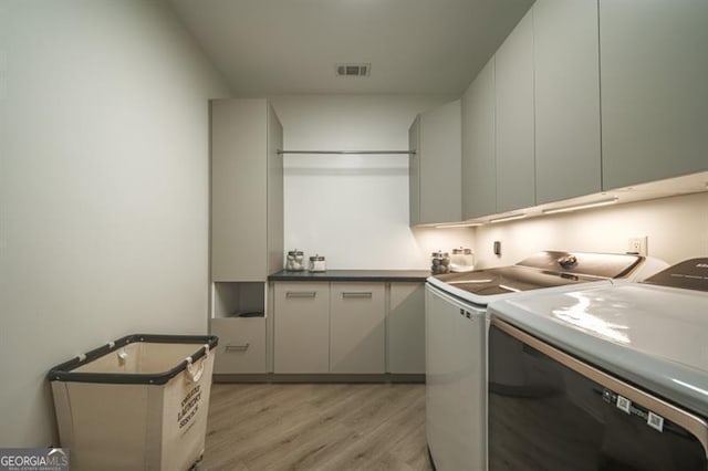 clothes washing area with cabinets, separate washer and dryer, and light hardwood / wood-style floors