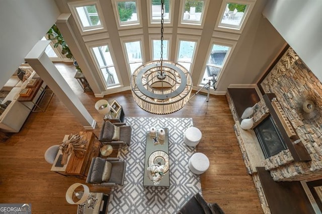 living room featuring dark hardwood / wood-style flooring, a notable chandelier, a towering ceiling, and a stone fireplace