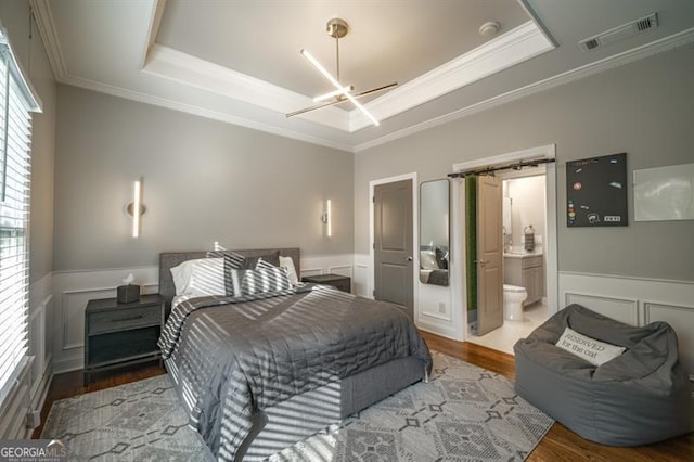 bedroom with ensuite bath, ornamental molding, a raised ceiling, and hardwood / wood-style floors