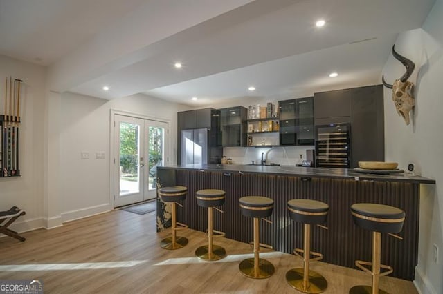 bar featuring stainless steel refrigerator, sink, beverage cooler, light hardwood / wood-style floors, and french doors