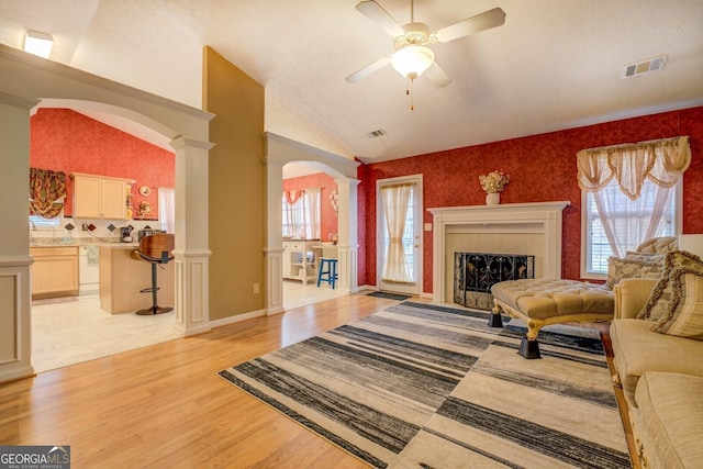 living room featuring light wood-type flooring, ornate columns, ceiling fan, and lofted ceiling