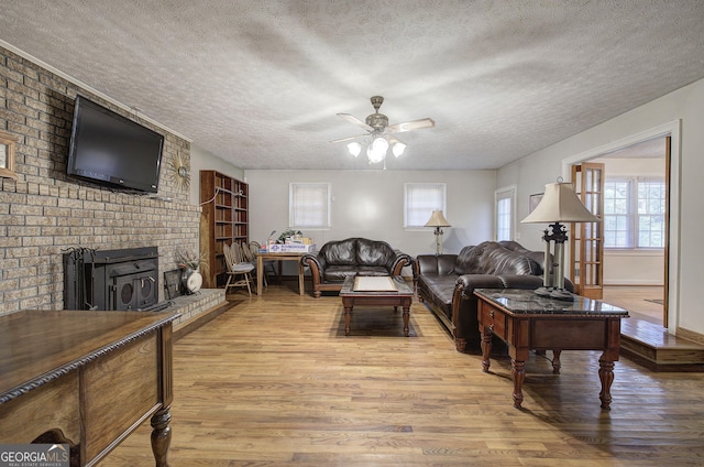 living room with ceiling fan, a wood stove, a textured ceiling, and light hardwood / wood-style flooring