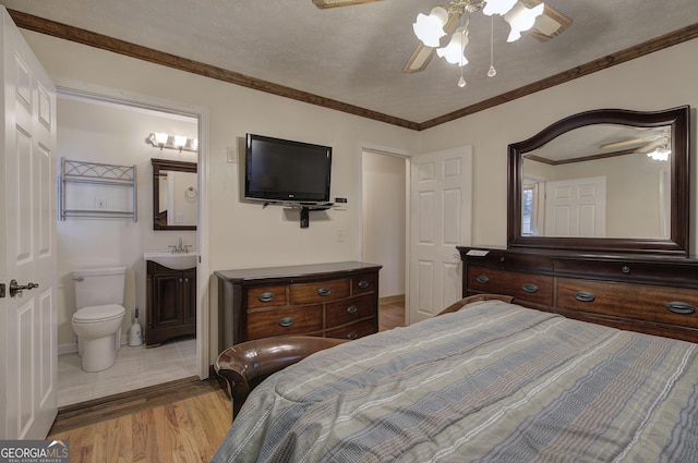 bedroom featuring a textured ceiling, ceiling fan, sink, light hardwood / wood-style flooring, and connected bathroom