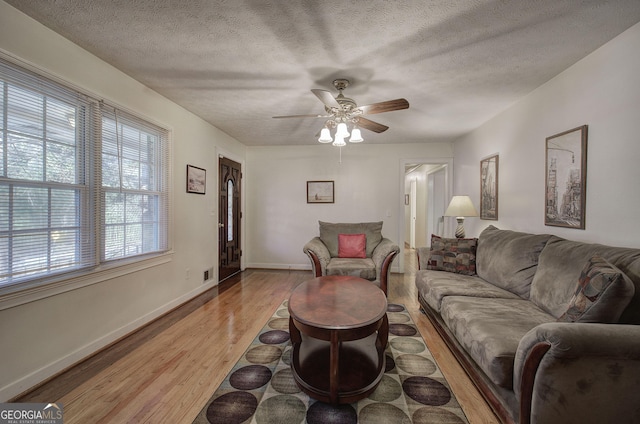 living room with ceiling fan, a textured ceiling, and light hardwood / wood-style flooring