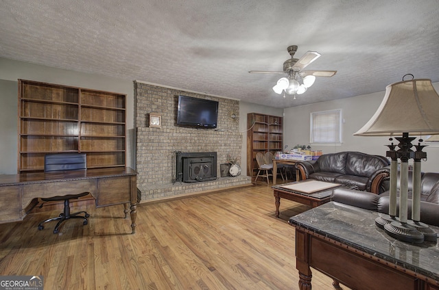 living room featuring a textured ceiling, light hardwood / wood-style flooring, a wood stove, and ceiling fan