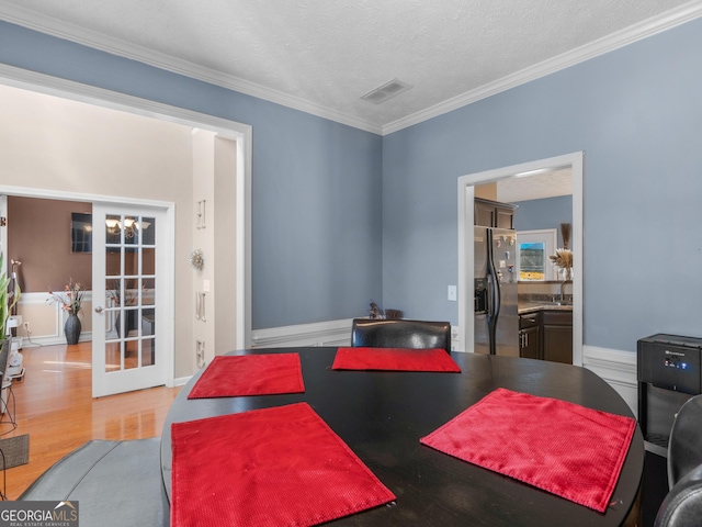 dining room with wood-type flooring, a textured ceiling, french doors, and ornamental molding