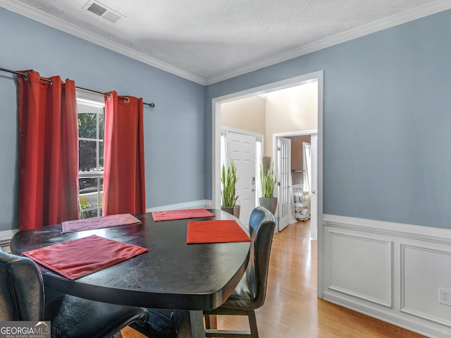 dining area with light hardwood / wood-style floors, ornamental molding, and a textured ceiling