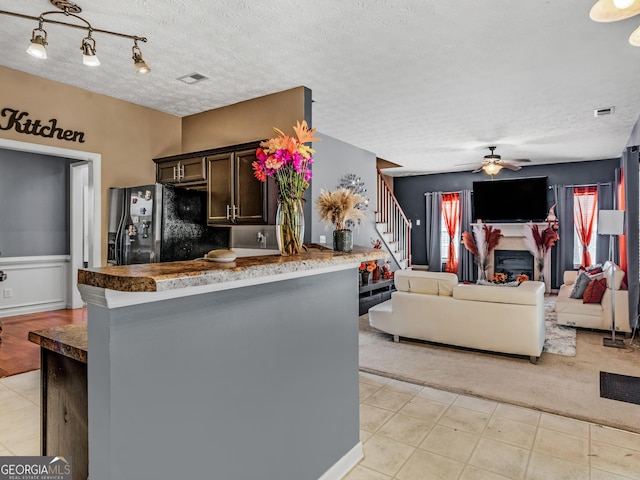 kitchen with kitchen peninsula, stainless steel fridge, dark brown cabinets, a textured ceiling, and ceiling fan