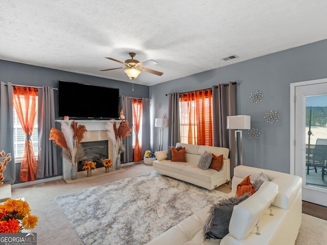 living room featuring ceiling fan, plenty of natural light, a textured ceiling, light carpet, and a fireplace