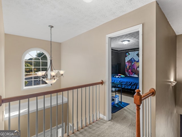 corridor featuring carpet flooring, a textured ceiling, and an inviting chandelier