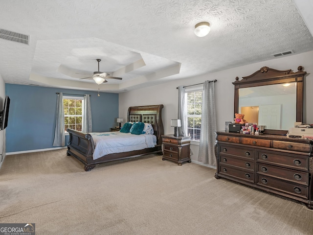 carpeted bedroom featuring a raised ceiling, multiple windows, and ceiling fan