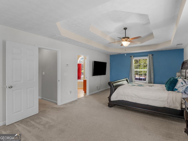 carpeted bedroom with a textured ceiling, a tray ceiling, ceiling fan, and ensuite bathroom