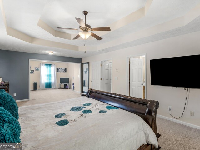 carpeted bedroom with a raised ceiling and ceiling fan