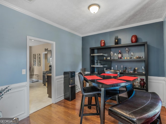 dining space featuring light hardwood / wood-style floors, ornamental molding, and a textured ceiling