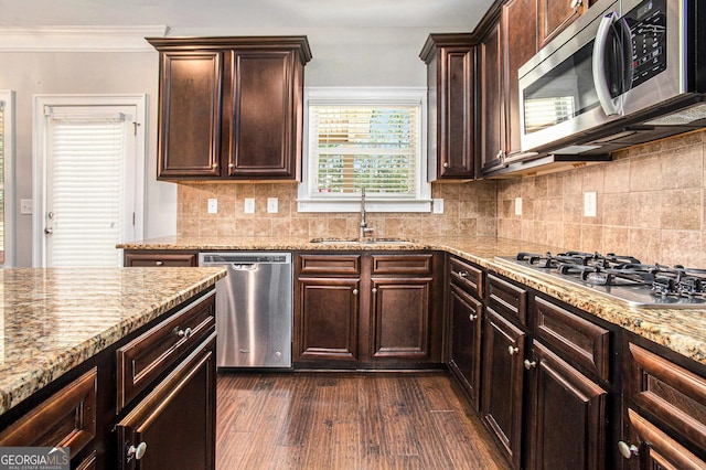 kitchen with sink, dark wood-type flooring, stainless steel appliances, light stone counters, and ornamental molding