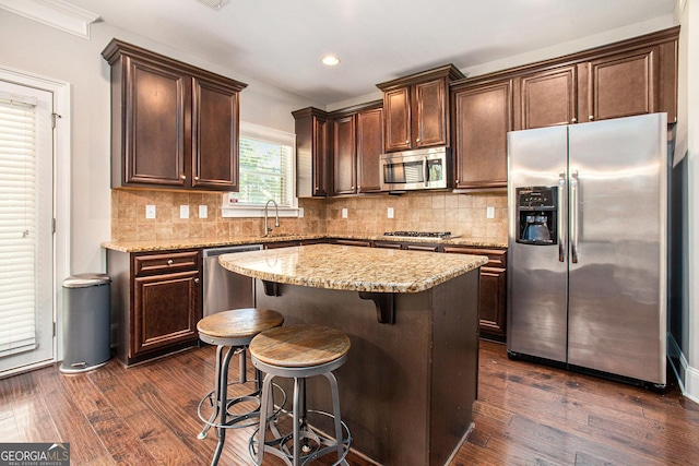 kitchen featuring dark wood-type flooring, stainless steel appliances, light stone counters, backsplash, and a kitchen island