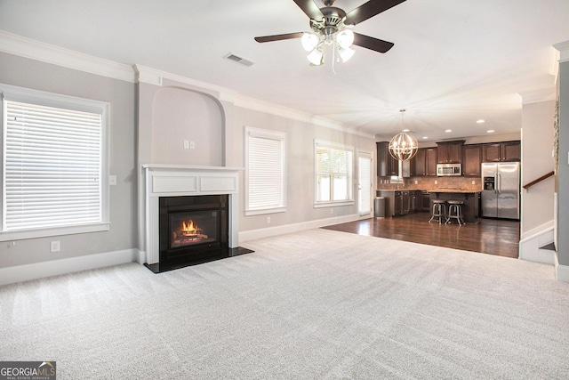 living room featuring dark colored carpet, ceiling fan with notable chandelier, and ornamental molding