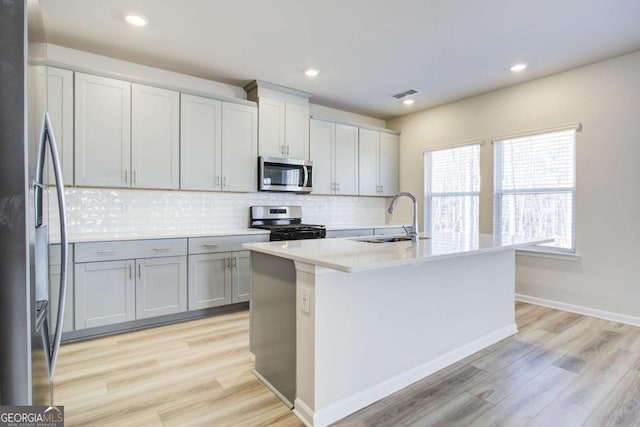 kitchen featuring a kitchen island with sink, sink, stainless steel appliances, and light hardwood / wood-style flooring