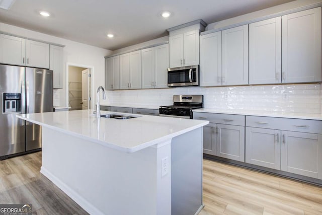 kitchen with backsplash, stainless steel appliances, sink, light hardwood / wood-style floors, and an island with sink