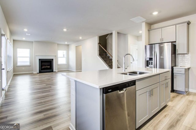 kitchen with appliances with stainless steel finishes, gray cabinetry, and an island with sink