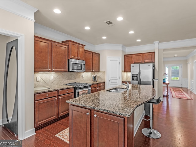 kitchen featuring sink, crown molding, dark stone counters, a center island with sink, and appliances with stainless steel finishes