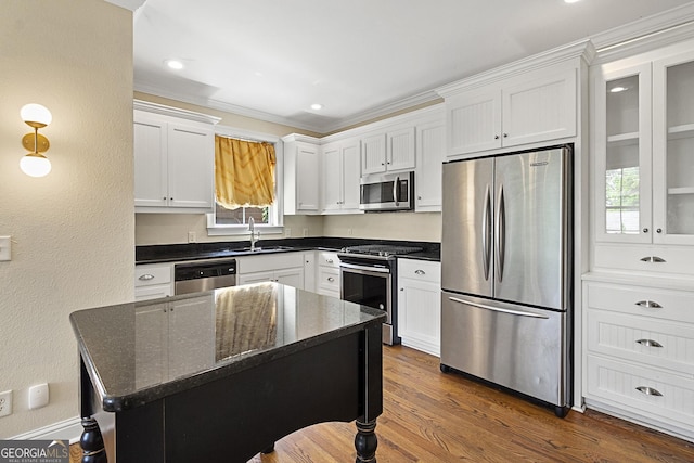 kitchen with appliances with stainless steel finishes, sink, dark stone countertops, white cabinets, and a center island