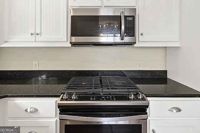 kitchen with stainless steel appliances, white cabinetry, and dark stone counters