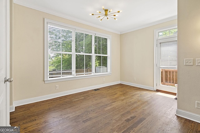 spare room with dark hardwood / wood-style flooring, an inviting chandelier, a wealth of natural light, and ornamental molding