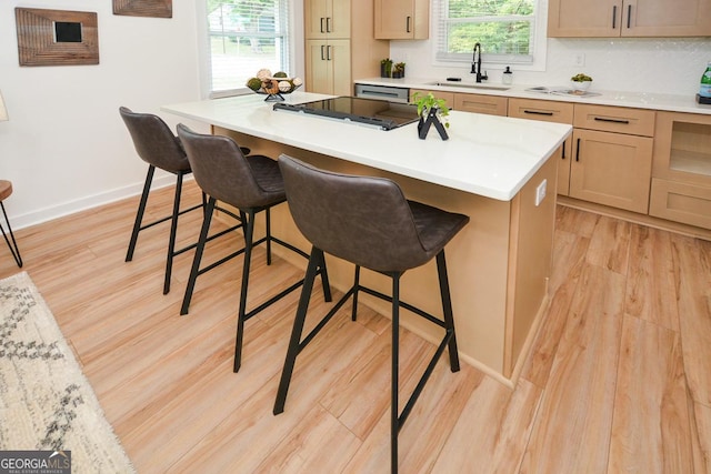 kitchen featuring light brown cabinets, sink, light hardwood / wood-style flooring, a kitchen island, and a kitchen bar