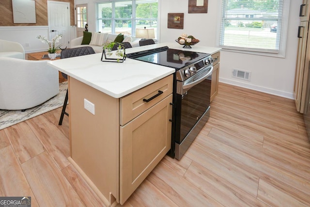 kitchen featuring light brown cabinetry, stainless steel range with electric stovetop, a breakfast bar area, and a healthy amount of sunlight